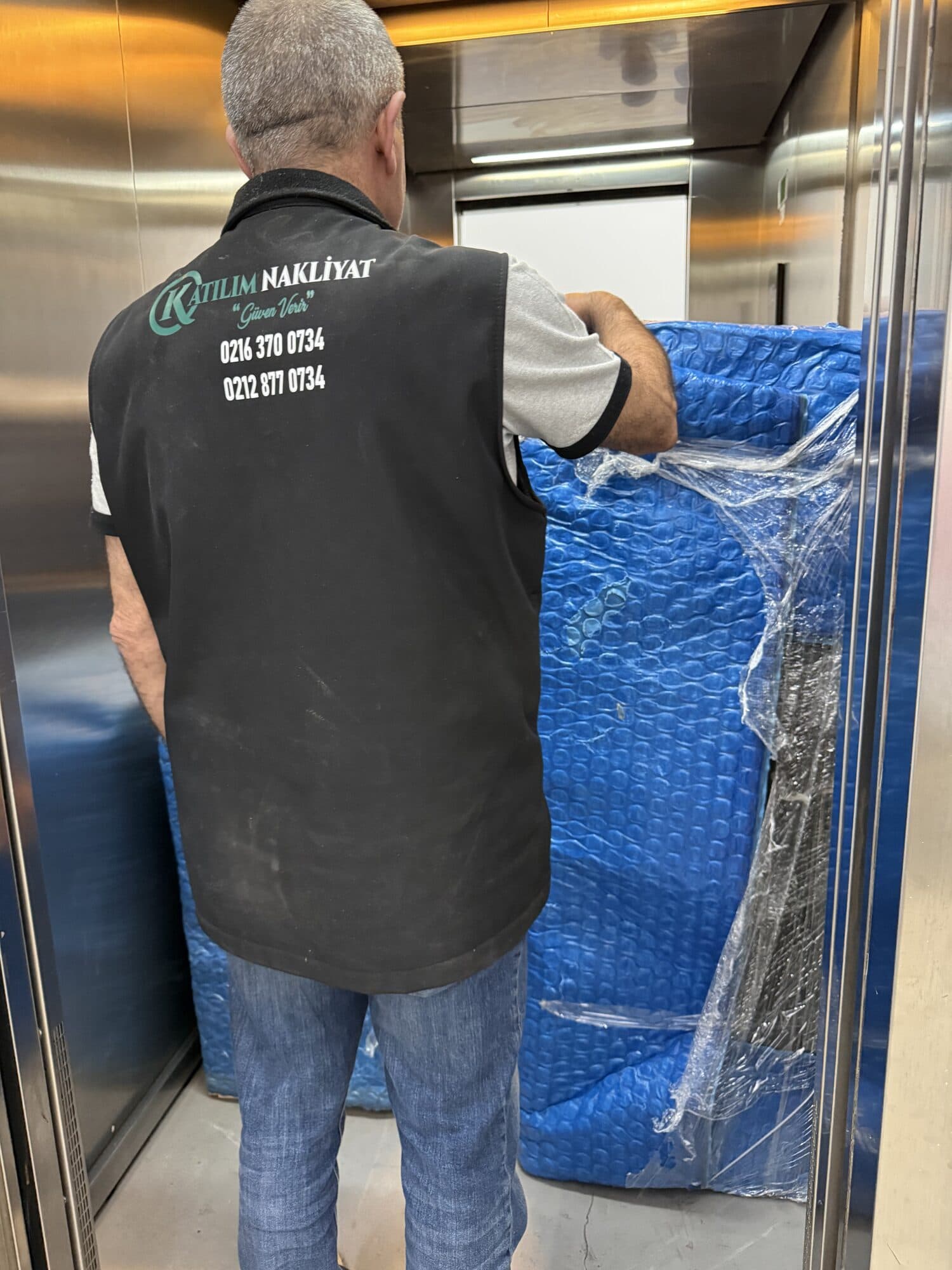 Paketlenmiş eşyayı asansörde taşıyan Katılım Nakliyat personeli